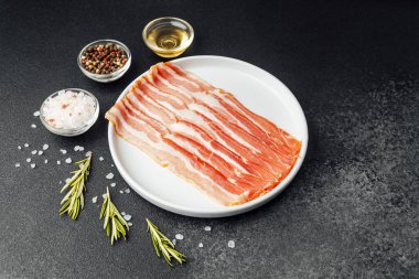 Beyaz tabakta çiğ domuz pastırması, biber, tuz ve biberiye.