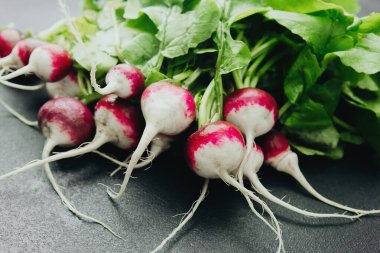 Siyah arka planda yeşil yapraklı taze kırmızı turplar.