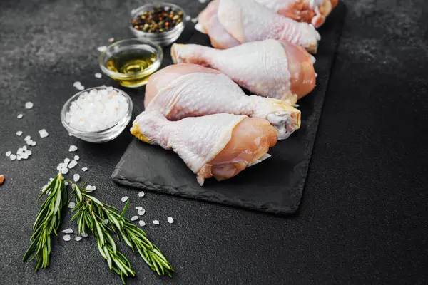 Siyah tahta üzerine yerleştirilmiş tavuk budu, otlar ve tuzlu.