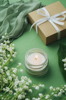 Kavanozda mum alevi, vadi çiçekli beyaz zambak ve yeşil arka planda hediye kutusu.