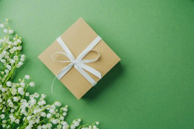 Beyaz kurdeleli bir hediye kutusu ve yeşil arka planda vadi çiçekleri.