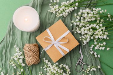 Çiçekler arasında kurdeleli bir hediye kutusu ve yeşil arka planda rahat bir mum.