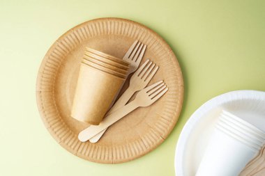 Yeşil zemin üzerine dağılmış çevre dostu kağıt bardaklar ve çatallar