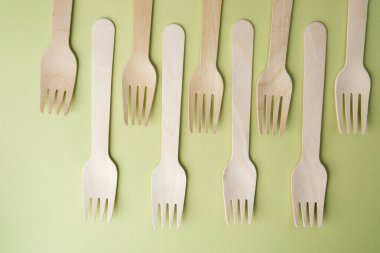 Pastel yeşil arka planda tek kullanımlık ahşap çatallar.