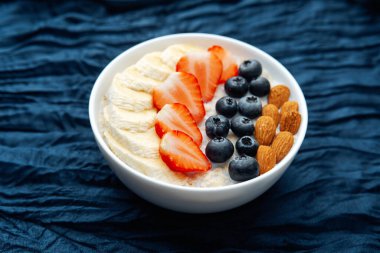 Koyu mavi tekstil arka planında meyveler ve bademlerle yulaf ezmesi kasesi
