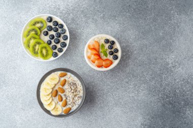 Çeşit çeşit yulaf ezmesi kaseleri ve gri masada fındık ve chia tohumları.