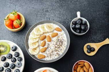Çeşit çeşit kahvaltı yulaf ezmesi kaseleri, içinde meyve çili tohumları ve siyah arka planda bademler var.