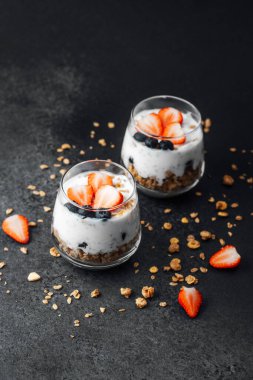 Yoğurtlu granola parfe, koyu arkaplanda çilek ve yabanmersini.