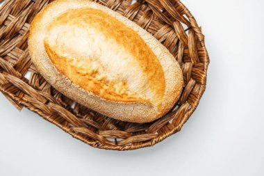 Kabuklu bir somun ekmek dokuma sepetinde düz bir arkaplanda duruyor..