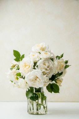 Beyaz masadaki cam vazoda bej desenli duvar arkaplanı olan beyaz gül buketi.
