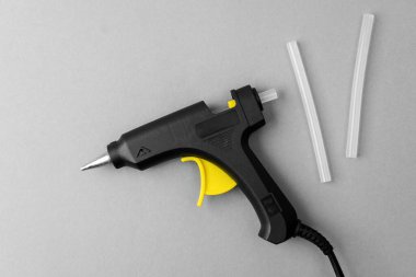 Glue gun with sticks on gray background