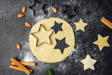 Yemek blogu ve mevsimlik tarif konsepti için karanlık masa üzerinde un ve malzemelerle pişirilmiş Noel yıldızı kurabiyeleri.