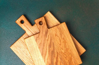 Üç pürüzsüz tahta kesme tahtası koyu bir tezgahta sergilenir..