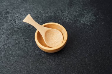 Küçük ahşap bir kase ve eşleşen bir kaşık koyu dokulu bir yüzey üzerinde duruyor..