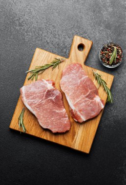 Sulu domuz pirzolası ahşap bir kesme tahtasının üzerinde biberiye ve biberle dinleniyor.