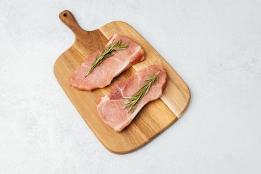 İki biberiyeli domuz pirzolası kesme tahtasına oturmuş, pişirmeye hazır..