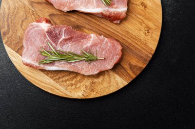 Ağaç kesme tahtasına biberiyeli iki çiğ domuz pirzolası..