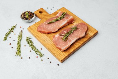 İki domuz pirzolası baharat ve otlarla tatlandırılmış bir kesme tahtasında sergilenir..