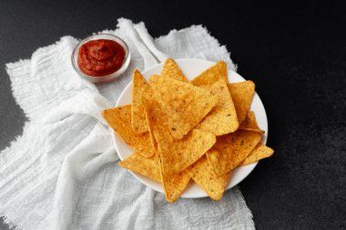 Beyaz kumaş ve siyah arkaplanda domates soslu Nacho cipsi.