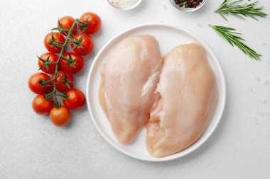Çiğ tavuk göğsü, beyaz tabakta otlar ve domateslerle yakın plan.