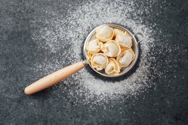 Mutfak arka planında süzgeçte un tozlu cappelletti makarna.