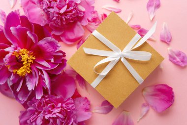 Beyaz kurdeleli hediye kutusu ve pastel arka planda pembe şakayıklar.