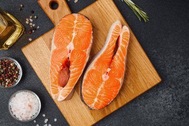 Baharatlarla çevrili ahşap bir tahtanın üzerinde sunulmuş iki somon filetosu..