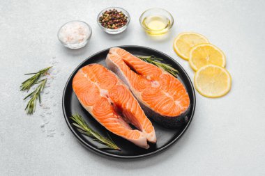 İki somon filetosu siyah bir tabakta limon dilimleri ve otlarla sıralanır..