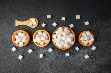 Şeker küpleriyle dolu çeşitli ahşap kaseler koyu bir yüzeyde sergilenir..