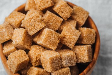 Kahverengi şeker küpleriyle dolu ahşap bir kase dokulu bir yüzeye dayanır..