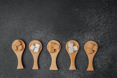 Tahta kaşıklardaki şeker küpleri koyu bir arka plana vurgu yapar..