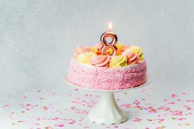 Hoş pembe bir doğum günü pastası, kıvrımları ve bir '8' mumu standın üzerinde duruyor..