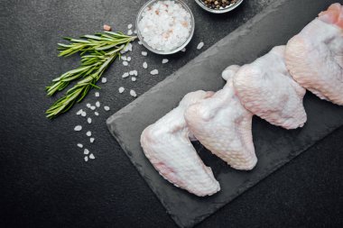 Siyah tahtada çiğ tavuk kanadı ve baharat.