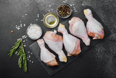 Siyah tahta üzerine yerleştirilmiş tavuk budu, otlar ve tuzlu.