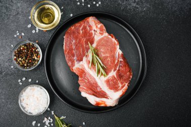 Çiğ biftek, otlar ve siyah tabakta baharatlar.