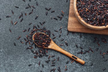 Tahta kasede siyah pirinç kaşık ve koyu arka planda dağınık taneler.