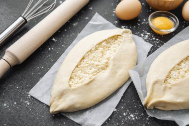 Malzemelerin üst görüntüsü ve iki pişmemiş khachapuri un kaplı siyah masa üzerinde
