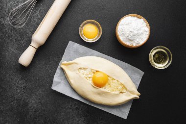 Parşömen üzerinde peynir ve sarısı olan Khachapuri ve koyu mutfak masası.