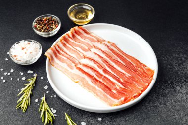 Beyaz tabakta çiğ domuz pastırması, biber, tuz ve biberiye.