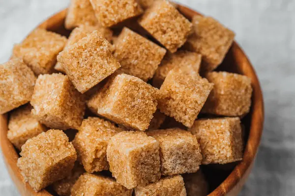 Kahverengi şeker küpleriyle dolu ahşap bir kase dokulu bir yüzeye dayanır..