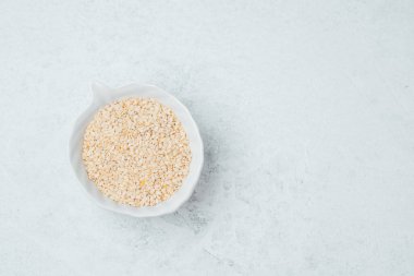 Açık gri bir yüzeye yerleştirilmiş susam tohumlarıyla dolu bir kase..