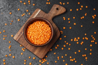 Mercimek ahşap bir kaseye konur. Etrafı karanlık bir yüzeye saçılmış parçalarla çevrilidir..