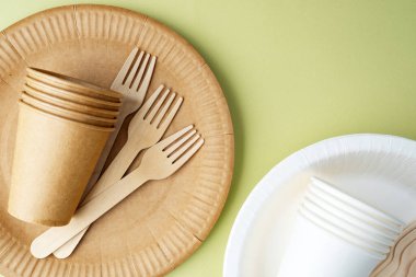 Yeşil zemin üzerine dağılmış çevre dostu kağıt bardaklar ve çatallar