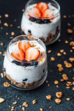 Yoğurtlu granola parfe, koyu arkaplanda çilek ve yabanmersini.