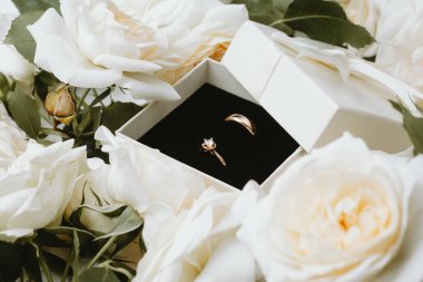 Altın evlilik ve nişan yüzükleri beyaz güllerle çevrili kutuda.