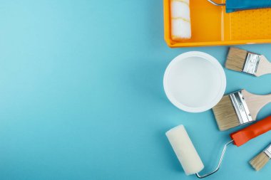 Yaratıcı dekorasyon ve DIY yenileme konsepti için Cyan arkaplan üzerinde düz boya araçları ve kova yatar