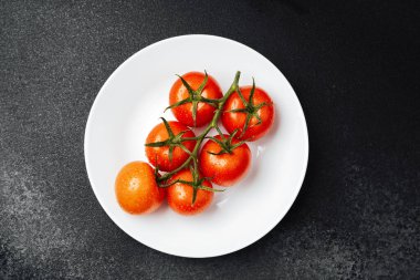 Parlak kırmızı domatesler beyaz bir tabakta, su damlacıklarıyla parlıyorlar..