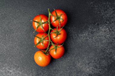 Koyu bir arka planda duran yeşil saplı canlı kırmızı domates kümesi..