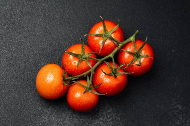 Yeşil saplı olgun kırmızı domatesler ve siyah bir yüzey üzerinde su damlacıkları..