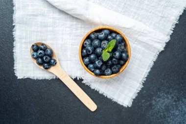 Bir kasede olgun yaban mersini ve desenli bir yüzeye yerleştirilmiş nane filizi..